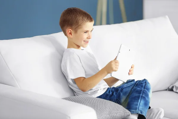 Chłopiec z tabletu, siedząc na kanapie — Zdjęcie stockowe