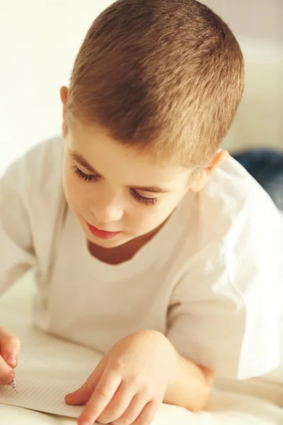 Kleine jongen schrijven in notitieblok — Stockfoto