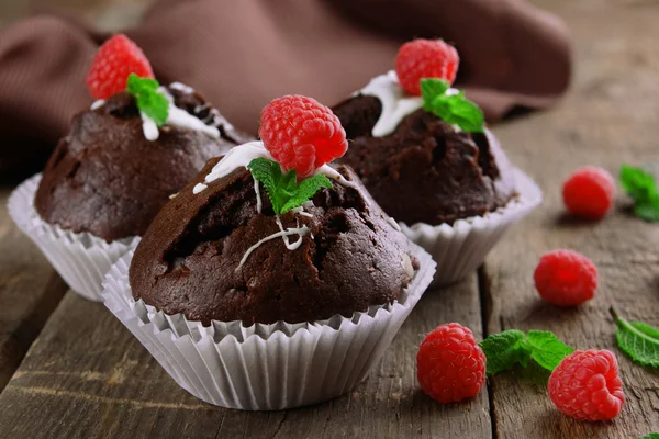 Deliciosos cupcakes de chocolate con bayas y menta fresca en la mesa de madera de cerca — Foto de Stock