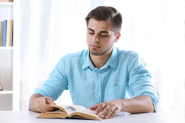 Jovem homem lendo livro à mesa — Fotografia de Stock