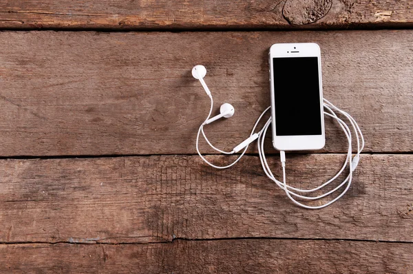 Celular branco com fones de ouvido em fundo de madeira — Fotografia de Stock