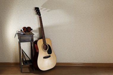 Akustik gitar dışkı ve kulaklıktan odasında duvarda propped