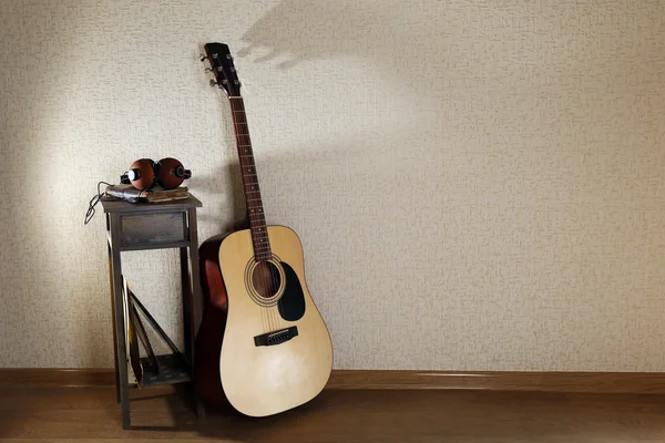 Guitarra acústica apoiada na parede com fezes e fones de ouvido na sala — Fotografia de Stock