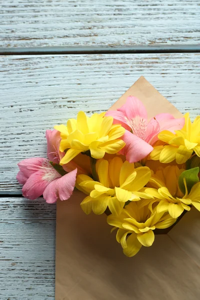 Pink alstroemeria and yellow chrysanthemum in envelope on wooden background — Stock Photo, Image