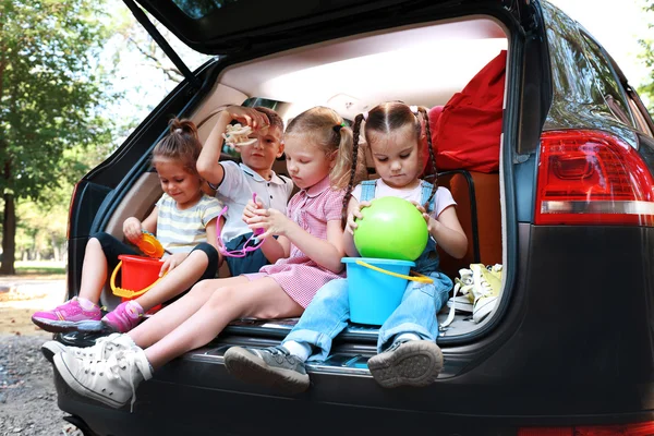 三个美丽的女孩和男孩坐在一辆车上的树干和笑 — 图库照片