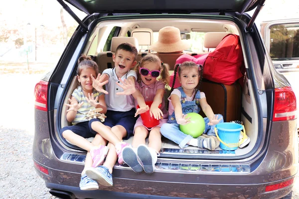 Tres hermosas chicas y un niño se sientan en el maletero de un coche y se ríen —  Fotos de Stock