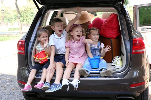 Trois belles filles et un garçon assis sur un coffre de voiture et riant — Photo