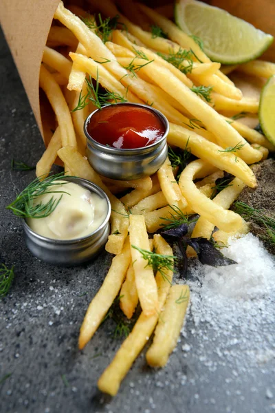 Franse frietjes in zak met saus, limoen en kruid op tafel — Stockfoto