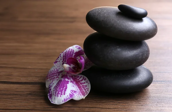 Schwarze Kiesel mit Orchidee auf hölzernem Hintergrund — Stockfoto