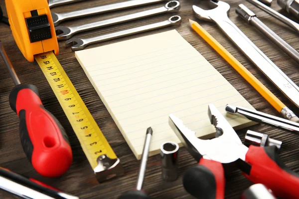 Diferentes tipos de herramientas con un cuaderno sobre fondo de madera, primer plano —  Fotos de Stock