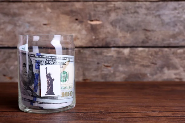 Rollo de billetes de dólar para diferentes necesidades en un frasco de vidrio sobre una mesa — Foto de Stock