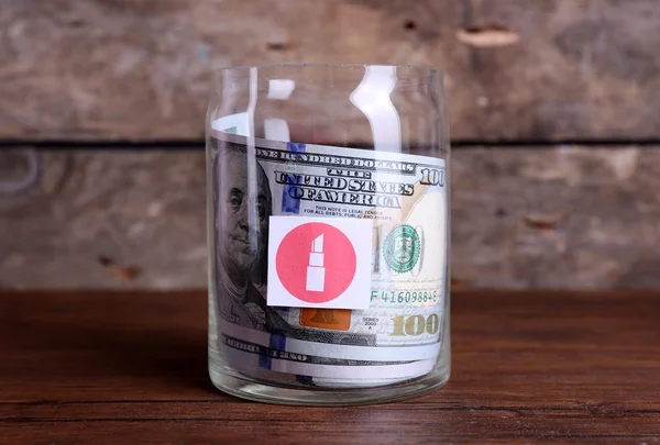 Rolo de notas de dólar para diferentes necessidades em um frasco de vidro em uma mesa — Fotografia de Stock