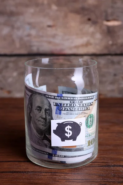 Rollo de billetes de dólar para diferentes necesidades en un frasco de vidrio sobre una mesa — Foto de Stock