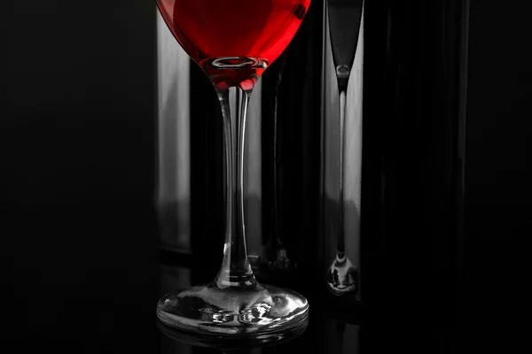 Red wine glass against bottles — Stock Photo, Image