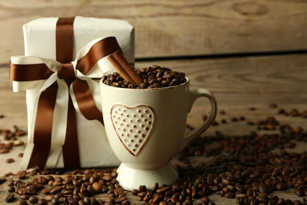 Hermoso regalo con arco y granos de café en taza, sobre fondo de madera —  Fotos de Stock