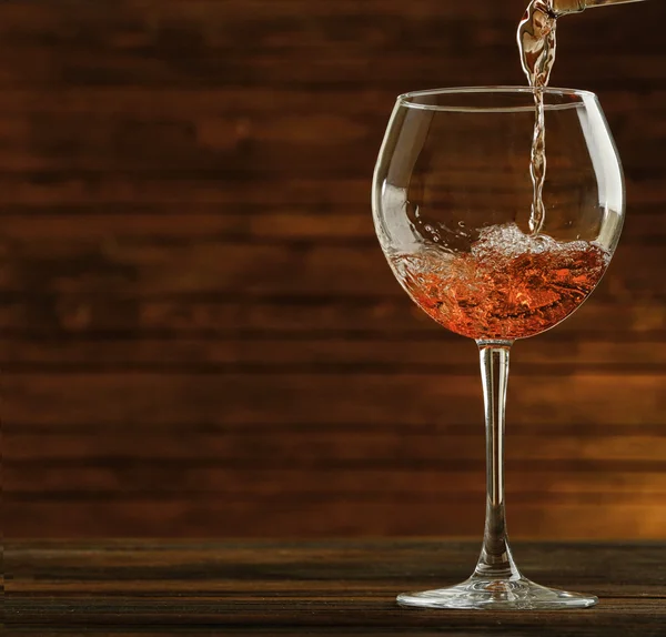 Rose wine pouring in glass on wooden background — Stock Photo, Image