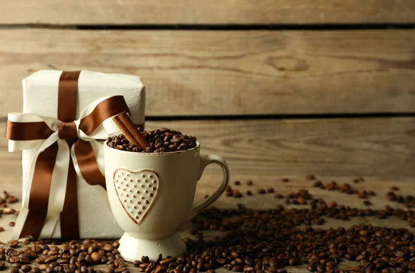 Bellissimo regalo con fiocco e chicchi di caffè in tazza, su sfondo di legno — Foto Stock