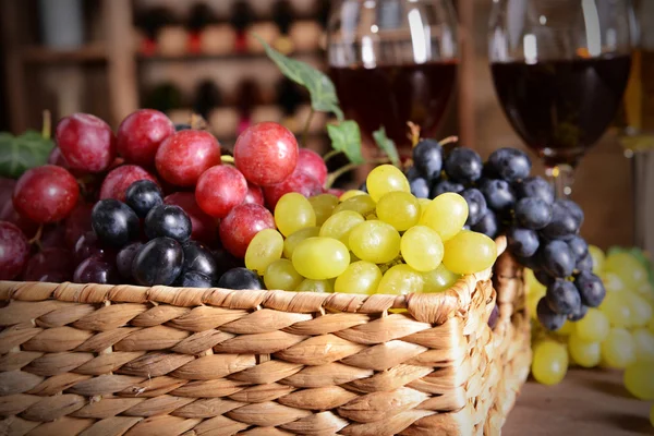 Grape in wicker box on a table on wine bottles background — Stock Photo, Image