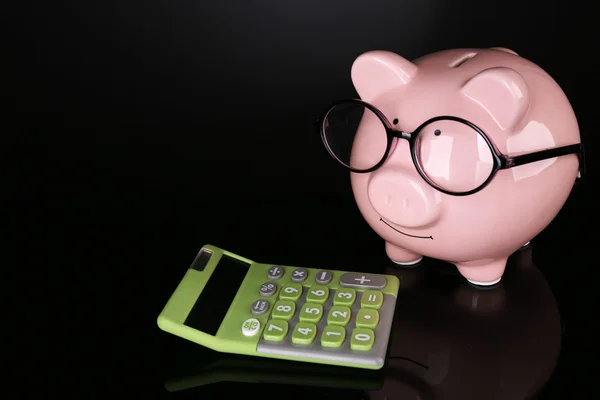 Sparschwein in Brille mit Taschenrechner auf dunklem Hintergrund — Stockfoto