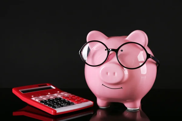 Piggy banco em óculos com calculadora no fundo escuro — Fotografia de Stock