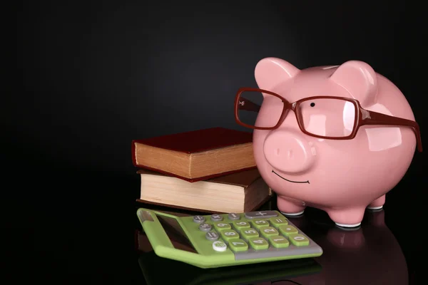 Piggy bank in glasses with calculator and books on dark background — Stock Photo, Image