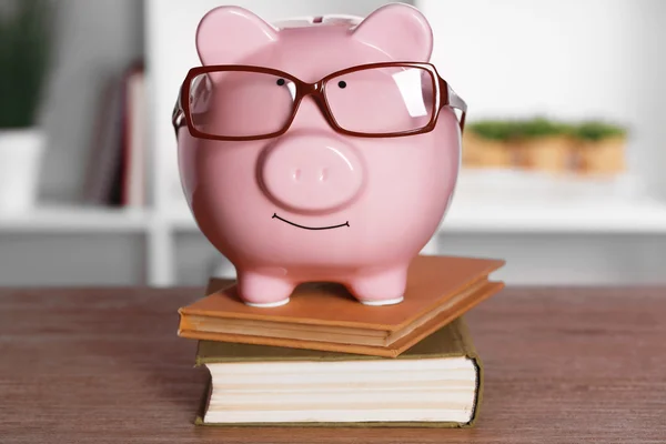 Piggy bank in glasses with books on home or office background