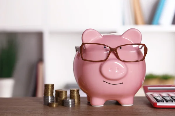 Piggy banco em óculos com calculadora e moedas em casa ou escritório fundo — Fotografia de Stock