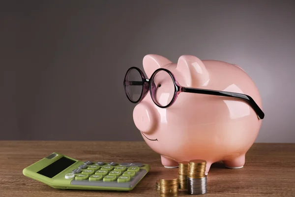 Sparschwein in Brille mit Taschenrechner und Münzen auf grauem Hintergrund — Stockfoto