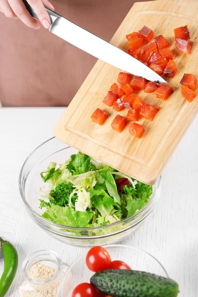Frauenhände fügen Lachsstücke in Schüssel mit Salat hinzu, Nahaufnahme — Stockfoto