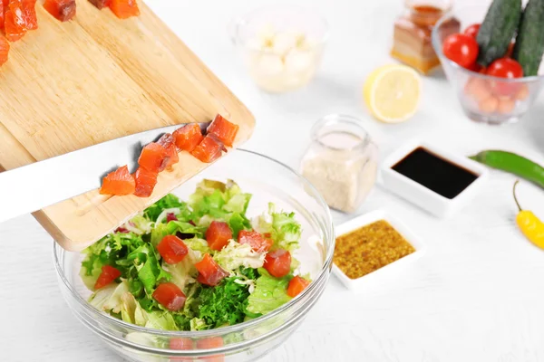 Frauenhände fügen Lachsstücke in Schüssel mit Salat hinzu, Nahaufnahme — Stockfoto