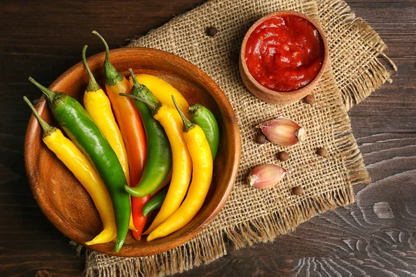 Pimentas, molho picante caseiro e especiarias em pano de saco, em fundo de madeira — Fotografia de Stock