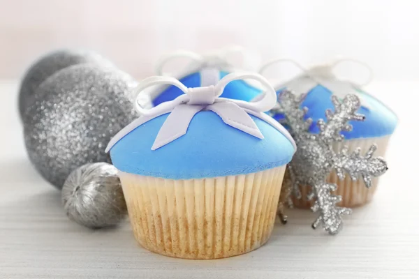 Tasty cupcakes with bow and Christmas toys on color wooden background — Stock Photo, Image