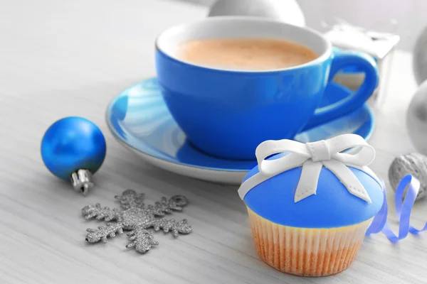 Gustoso cupcake con fiocco, tazza di caffè e giocattoli di Natale su sfondo di legno a colori — Foto Stock