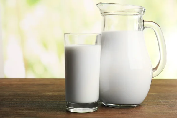 Leche en frasco y en vaso sobre mesa sobre fondo natural borroso — Foto de Stock