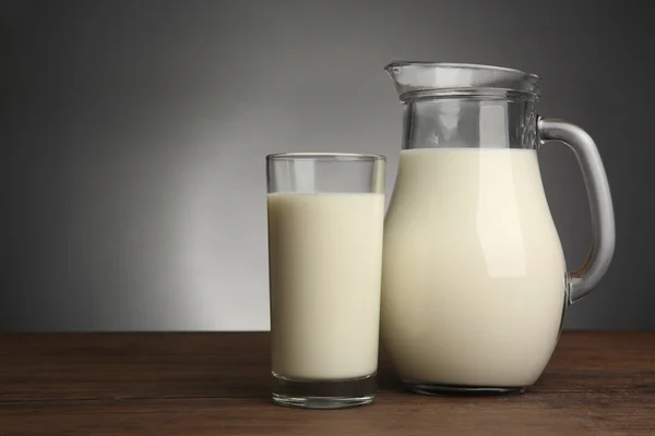 Melk in glazen en in pot op tafel op lichte achtergrond — Stockfoto