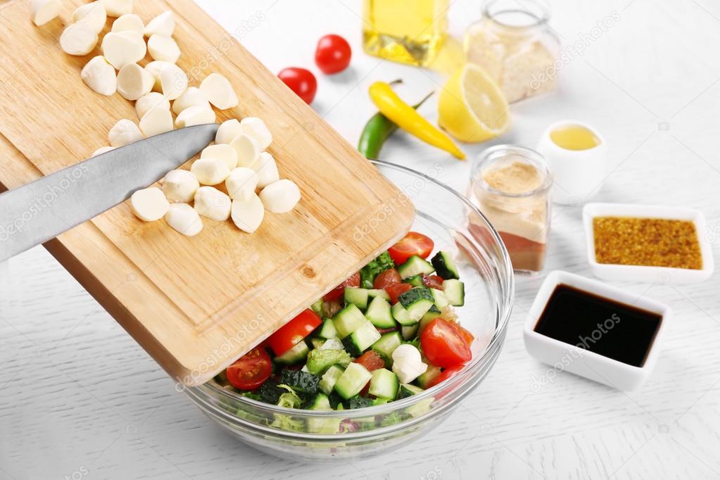 Female hands cutting mozzarella cheese for salad, at kitchen