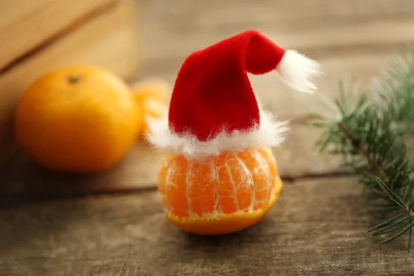 Mandarine mit kleinem Weihnachtsmann-Hut, auf altem Holztisch, Nahaufnahme — Stockfoto