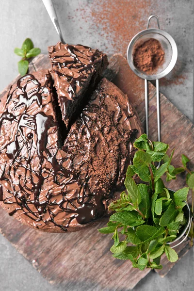 Sliced chocolate pie with pile of mint and sieve on cutting board — Stock Photo, Image