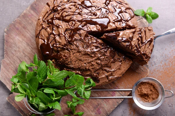 Sliced chocolate pie with pile of mint and sieve on cutting board — Stock Photo, Image