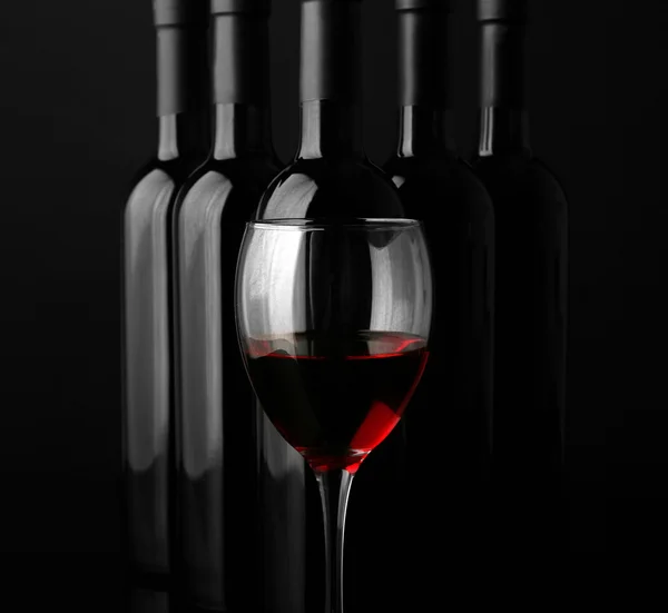 Red wine glass against bottles — Stock Photo, Image