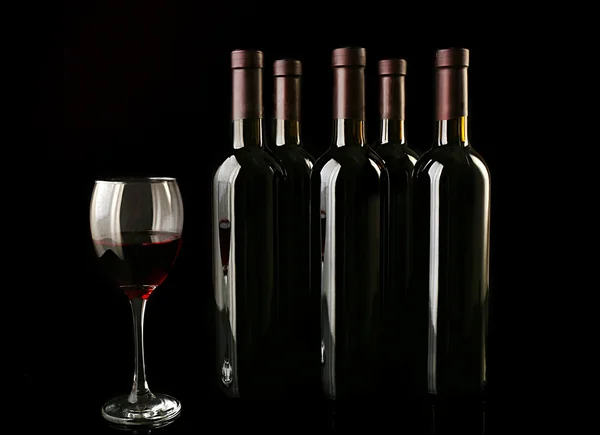 Red wine glass against bottles — Stock Photo, Image