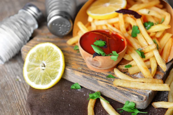 Papas fritas en papel artesanal sobre tabla de cortar — Foto de Stock