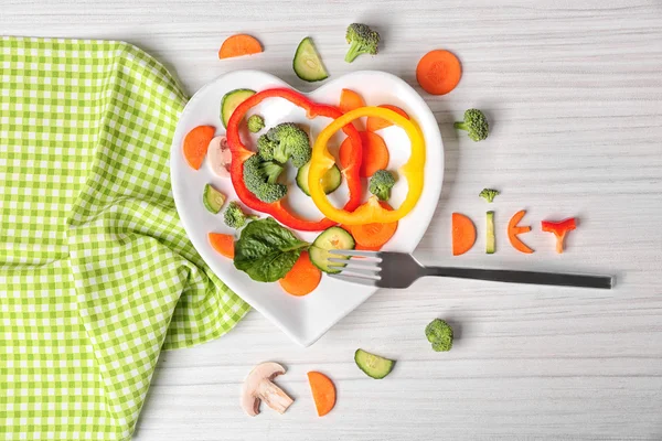 Verduras cortadas útiles en un plato en forma de corazón en vista superior de mesa de madera — Foto de Stock