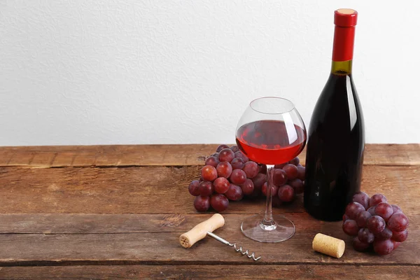 Wina i winogron na drewnianym stole przed jasnym tle — Zdjęcie stockowe