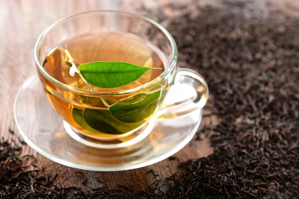 Glas kopje thee met groene bladeren op houten achtergrond versierd met verspreide thee — Stockfoto