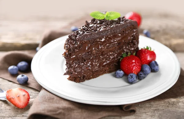 Torta al cioccolato con crema di cioccolato e bacche fresche su piatto, su fondo di legno — Foto Stock