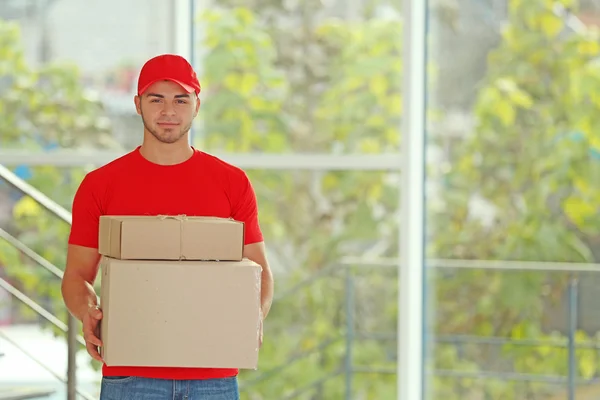 Kırmızı üniformalı postacı elinde bir paket tutuyor. — Stok fotoğraf