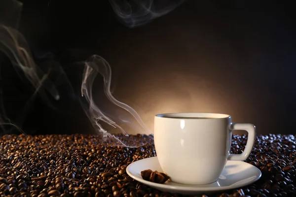 Taza de café caliente entre granos de café sobre fondo oscuro — Foto de Stock