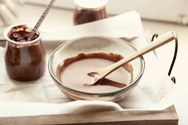 Chocolate derretido en cuenco de vidrio en bandeja, sobre fondo de madera — Foto de Stock