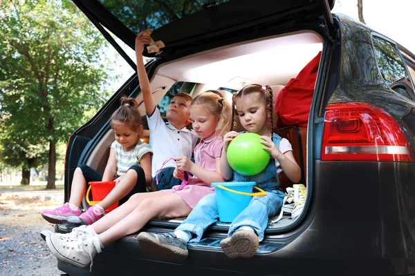 Trois belles filles et un garçon assis sur un coffre de voiture et riant — Photo